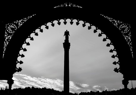 A statue stands on a pillar under a richly decorated archway