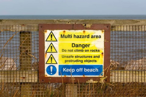 Environment Agency warning danger sign above rock armour, East Lane, Bawdsey, Suffolk, England, UK