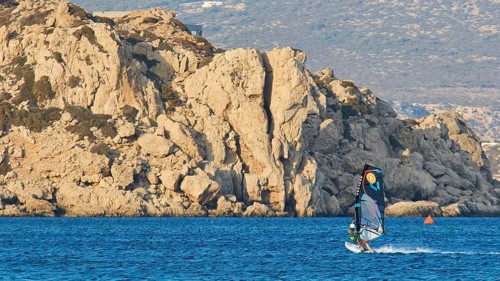 A single windsurfer rides along a rocky coast, windsurfer, Meltemi windsurfing spot, Devils Bay,