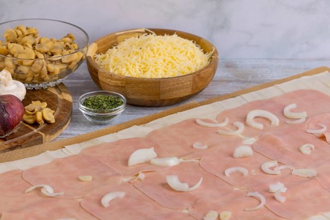 Ingredients such as cheese, onions, mushrooms next to strudel dough topped with ham