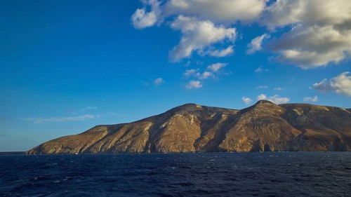 Rocky coast of an island under blue sky and light clouds, Kassos Island, neighbouring island