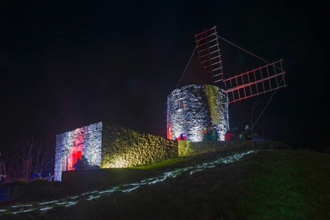 Historic windmill at night, illuminated with red and blue modern lights, on a hill, world of