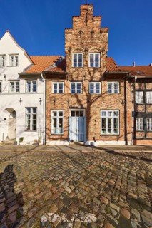 Historic brick building, façade with gable, windows, door and wall anchor, cobblestones, street An
