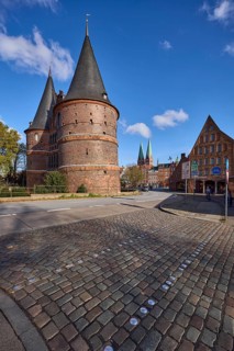 Lübeck Holstentor, side view, pedestrian crossing, cobblestone pavement, blue sky with fair weather