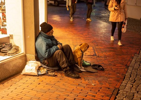 Homeless man with a dog sits in a shopping mall as people walk by in Husum, Schleswig-Holstein,