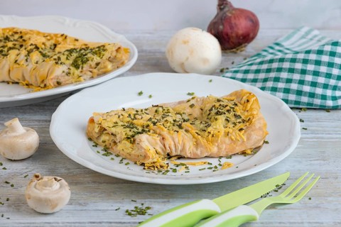 Ready-made savoury strudel with cheese and ham served on a plate, decorated with herbs