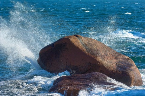 Large granite rose rock, in the middle of the sea, lapped by waves, with splashing spray against a
