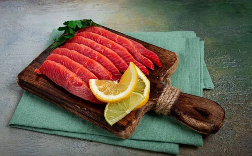 Chum salmon, cold smoked, sliced, on a cutting board, with lemon and parsley, top view, close-up,