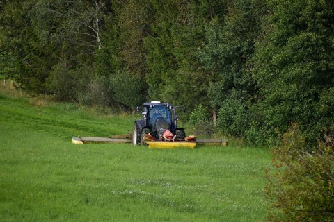Farmer with a Valtra tractor mowing at the edge of a forest with 3 mowers at the same time,