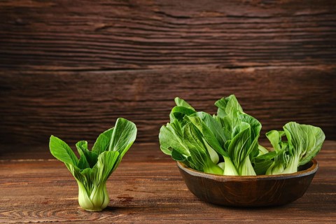 A collection of vibrant bok choy in a rustic wooden bowl on a wooden kitchen table, with one