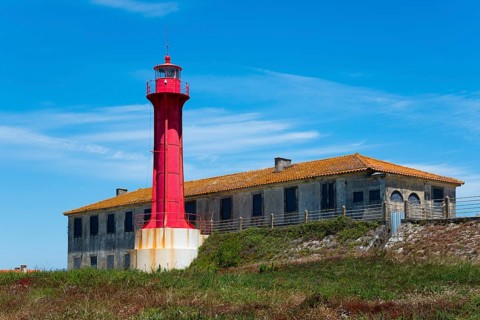 Red lighthouse next to a building in a coastal landscape with blue sky, Farol de Esposende in front