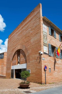 Modern museum building made of red bricks with blue shutters and the Spanish flag under a clear