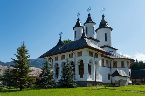 White orthodox church building with black roofs under a clear blue sky, Romanian Orthodox Monastery