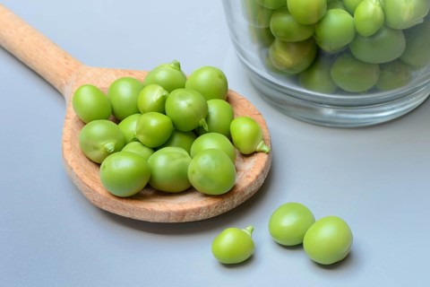 Fresh green peas in wooden spoon, Pisum sativum