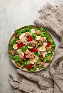 Tuna salad, vegetable salad with quail eggs, lettuce, red onion and cucumbers, on a light gray