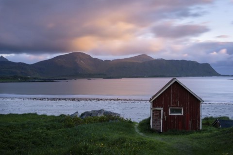A red wooden hut on the sandy beach of Ramberg (Rambergstranda), with the sea behind it. At night