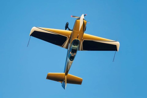 Golden stunt aerobatic plane performing stunts in blue sky. Concept of speed, difficulty,