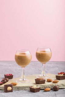 Sweet chocolate liqueur in glass with chocolate candies on a gray and pink background and stone