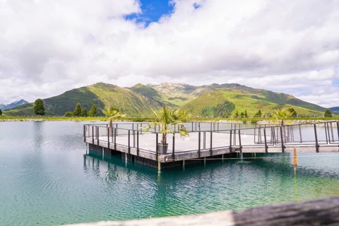 A tranquil lake with a pier, surrounded by a beautiful hilly and mountain landscape under a partly