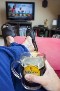 Couch potato, lazy man in comfy chair with pint of beer wearing worn slippers with big toes