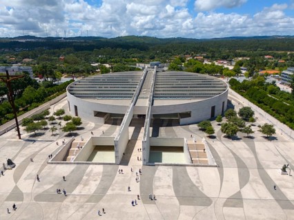 Modern architecture with a large square and people, surrounded by trees and forests, under a cloudy