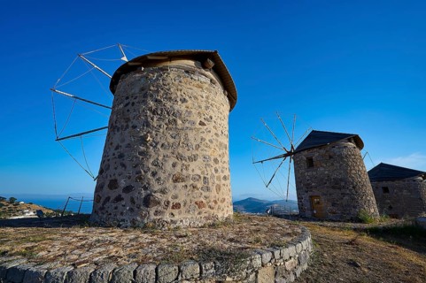 Two old stone windmills under a clear blue sky in a natural landscape, windmills, on a ridge, above