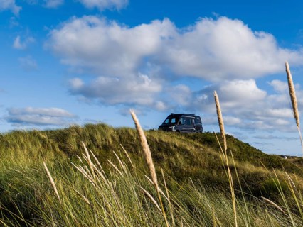 A campervan stands on a grassy dune under a blue sky with clouds, North Sea, Jutland, Denmark,