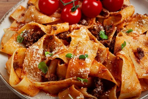 Pappardelle pasta with bolognese sauce, topped with parmesan cheese and cherry branch, homemade, no