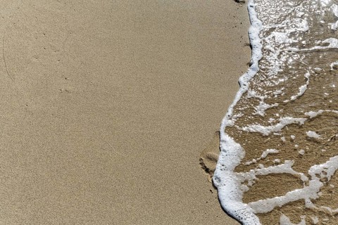 Gentle wave on the shore blurs footprint in the sand, Simos beach, text free space, symbolic photo,