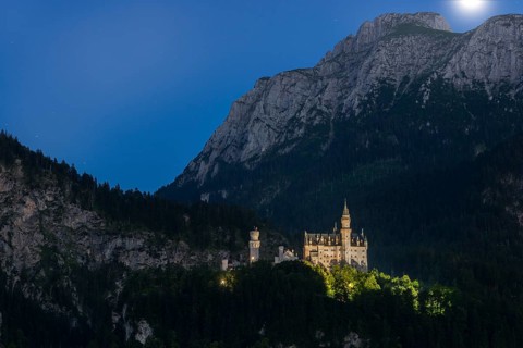 Neuschwanstein Castle in the mountains at night under a clear sky with moonlight, romantic,
