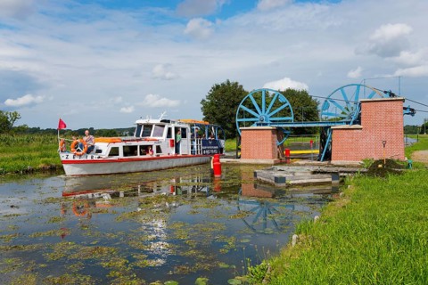 A boat passes a lock in a green landscape in sunny weather, ship Zefir, manoeuvrable wheels in the
