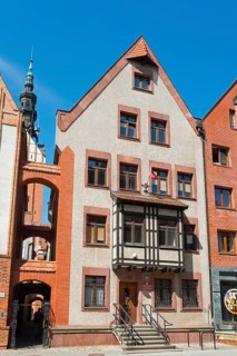 A historic half-timbered building with red brick elements and a high tower in the background under