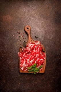 Prosciutto on a cutting board, top view, appetizer, breakfast, spices and herbs