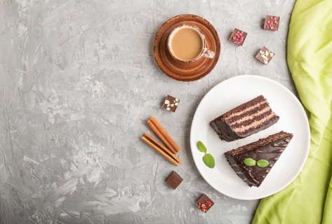 Homemade chocolate cake with milk cream and a cup of coffee on a gray concrete background with