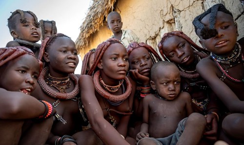Group of Himba children and young woman look at pictures on a camera, near Opuwo, Kaokoveld,