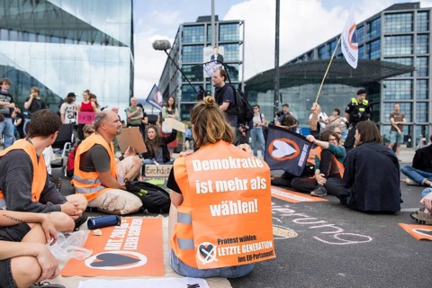 Last Generation activist with poster Democracy is more than voting! for the upcoming European
