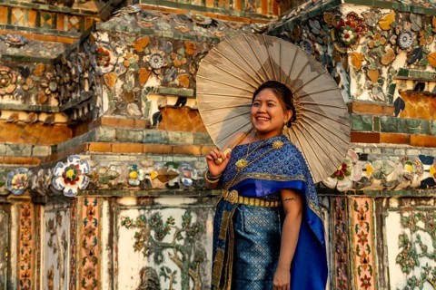 Traditionally dressed woman with umbrella poses in front of the temple Wat Arun or Temple of Dawn