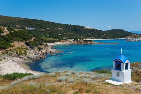 Small chapel with blue roof on a rocky coast with clear sea water, Greek Orthodox shrine, beach