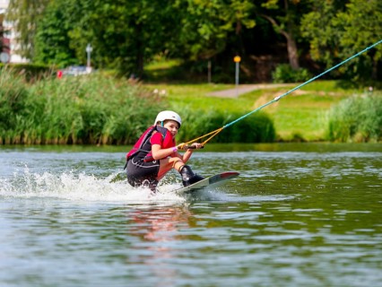 Boy or girl, water sports with wakeboard, red life jacket, water skiing in the wake park