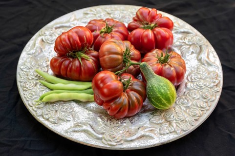 Tomatoes, ox hearts and a Vorgebirgstrauben pickled cucumber on a decorative plate on a black