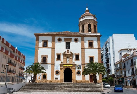 Large church with palm trees in the foreground, surrounded by urban buildings under a bright sky,