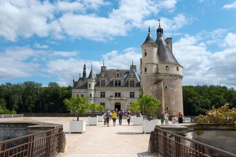 Tourists visiting a historic castle with a striking tower and blue sky in the background, Château