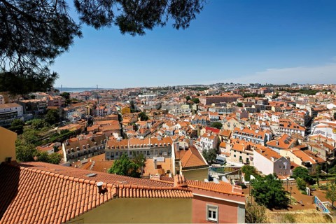 Panoramic view of Lisbon cityscape with terracotta rooftops under a clear blue sky, Lisbon