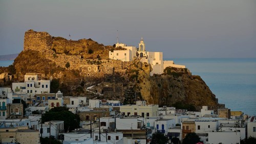 A historic castle and white houses on a hill overlooking the calm sea in the soft light of dawn,