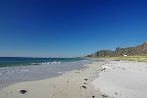 Beautiful beach with clear blue sky, gentle waves and mountains in the background, Bleik,