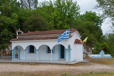 Small Greek church in a rural setting with flags and surrounding trees, located on the 77, island