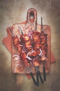 Pork kebab on skewers, with red onion, on a wooden chopping board, close-up, top view