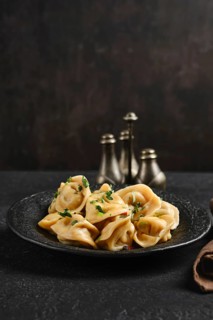 A black stone plate holds freshly made dumplings garnished with parsley, creating a delightful dish