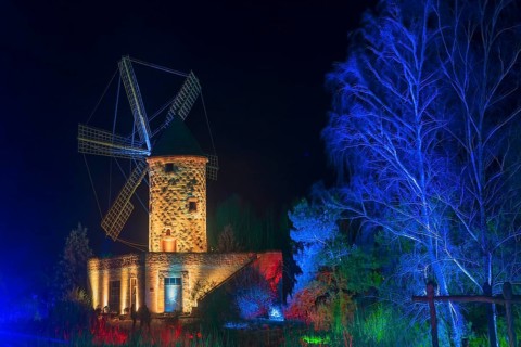 Historic stone mill at night, illuminated in blue, surrounded by trees, world of lights,