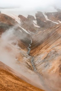 Steaming stream between colourful rhyolite mountains and snowfields, Hveradalir geothermal area,